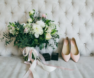 Wedding bouquet, pink bridal shoes and black boxes with rings on a luxury sofa. Indoors. Artwork