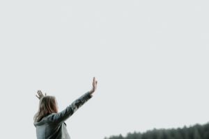 Woman standing alone outside with hands raised in worship