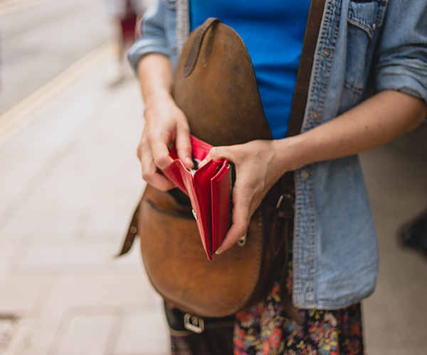 A young woman is standing in the street and is opening her purse to make a purchase