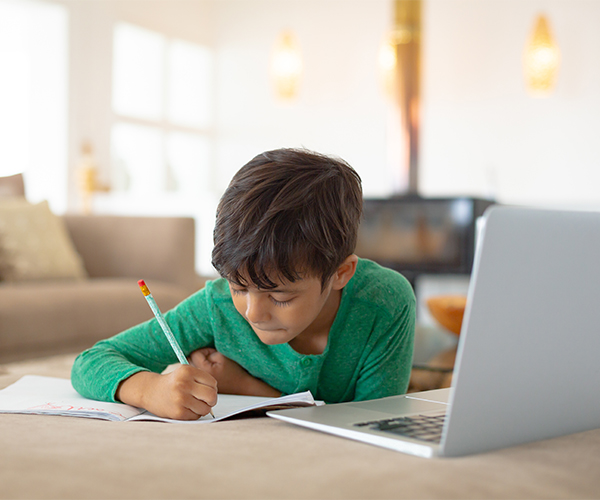 Boy using laptop while drawing a sketch on book at home